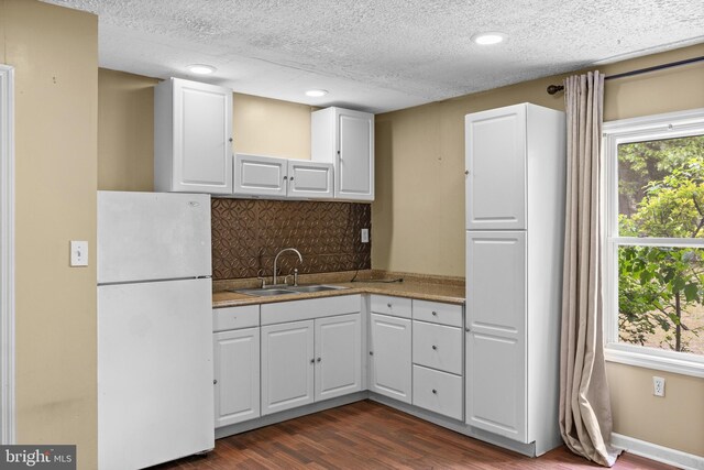kitchen featuring freestanding refrigerator, a sink, backsplash, dark wood-style floors, and white cabinets