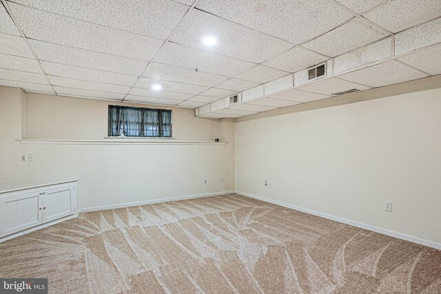 finished below grade area featuring a paneled ceiling, carpet flooring, baseboards, and visible vents