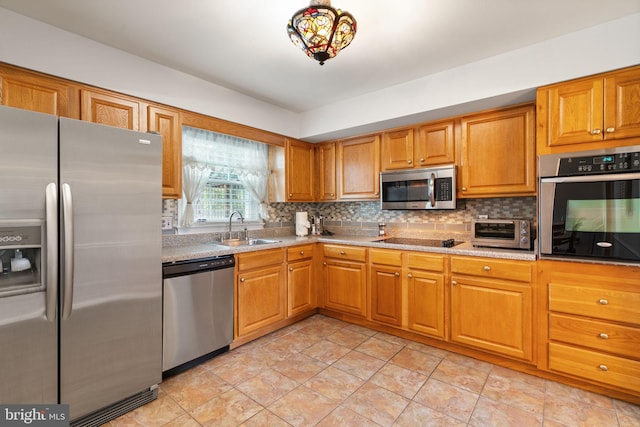 kitchen with appliances with stainless steel finishes, a sink, decorative backsplash, and brown cabinetry