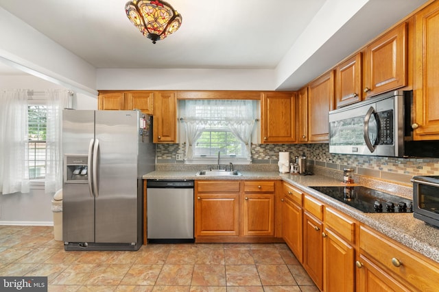 kitchen with stainless steel appliances, a sink, backsplash, brown cabinetry, and light countertops