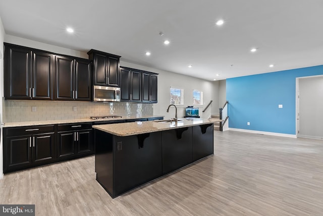 kitchen featuring appliances with stainless steel finishes, a sink, dark cabinets, an island with sink, and recessed lighting