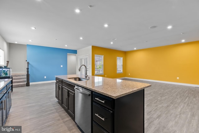 kitchen with a sink, dishwasher, open floor plan, light wood-style flooring, and dark cabinetry