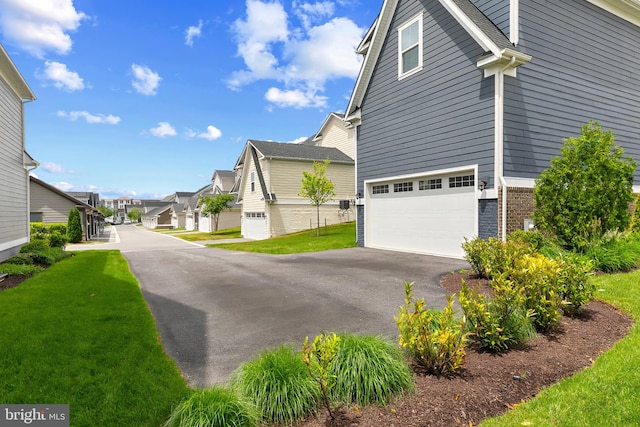 view of home's exterior with a garage, a yard, driveway, brick siding, and a residential view