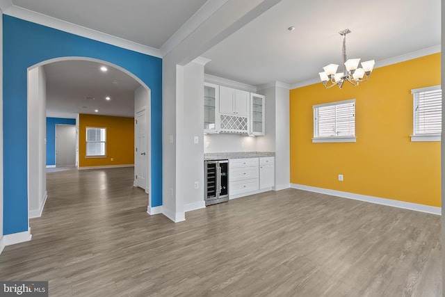 unfurnished living room with wine cooler, crown molding, arched walkways, a dry bar, and light wood-style flooring