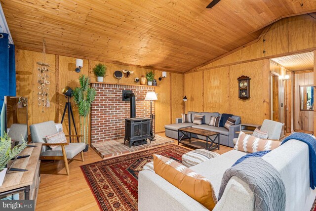 living room with a wood stove, lofted ceiling, wooden walls, wood finished floors, and wood ceiling