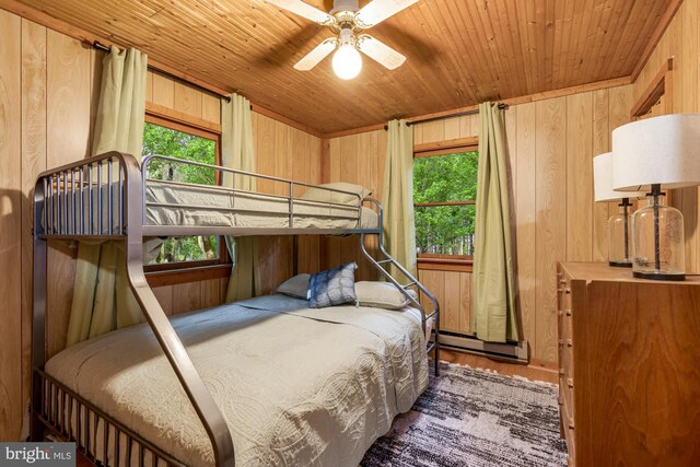 bedroom with a baseboard heating unit, multiple windows, wood ceiling, wood walls, and wood finished floors
