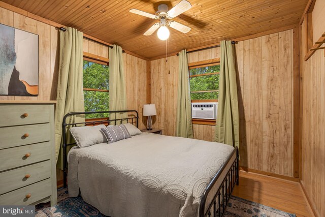 bedroom featuring multiple windows, wooden walls, wood finished floors, wooden ceiling, and cooling unit