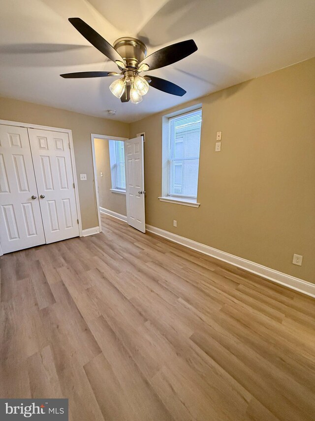 unfurnished bedroom with baseboards, wood finished floors, a closet, and ceiling fan