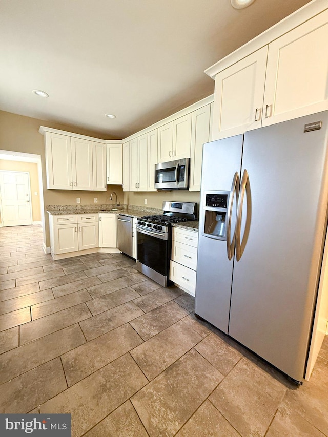 kitchen featuring stainless steel appliances, a sink, white cabinets, recessed lighting, and stone countertops