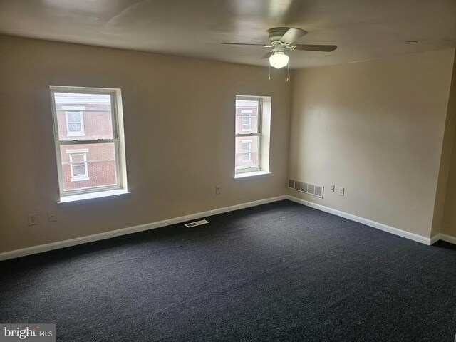 spare room featuring ceiling fan, dark colored carpet, and plenty of natural light