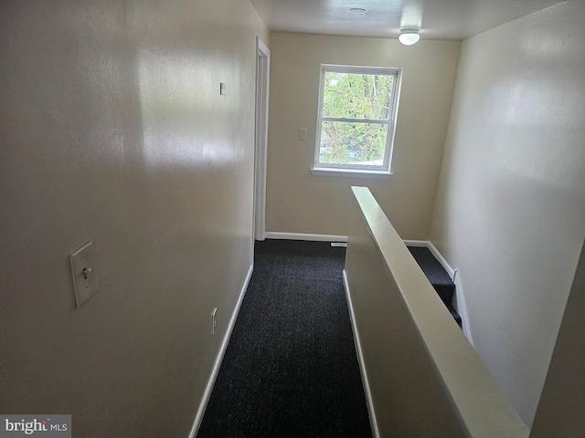 hall with an upstairs landing, baseboards, and dark carpet
