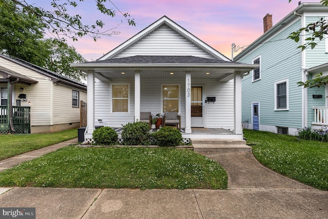 shotgun-style home with a porch, roof with shingles, and a lawn