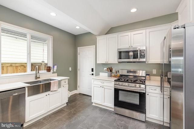 kitchen featuring lofted ceiling, a sink, light countertops, white cabinets, and appliances with stainless steel finishes