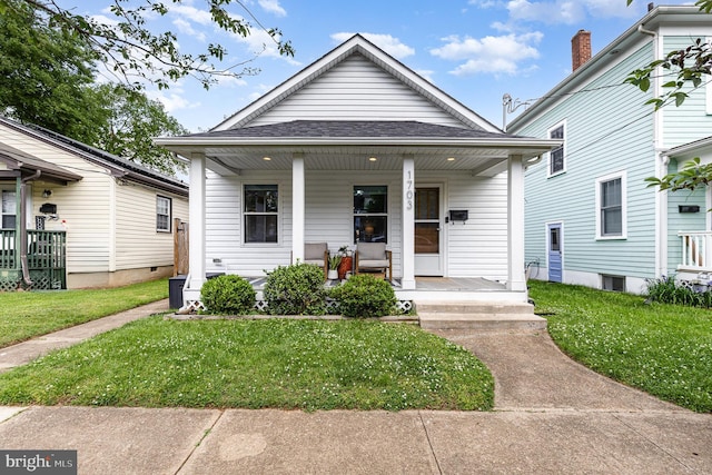 shotgun-style home featuring covered porch, roof with shingles, and a front yard