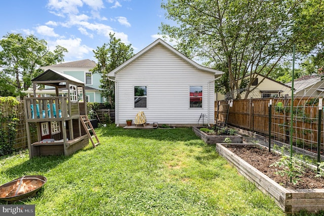 back of house featuring a yard, a fenced backyard, a fire pit, and a garden