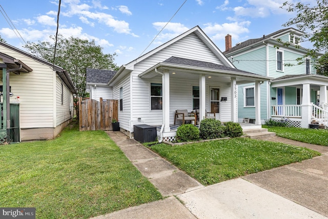 shotgun-style home featuring covered porch, roof with shingles, fence, and a front lawn
