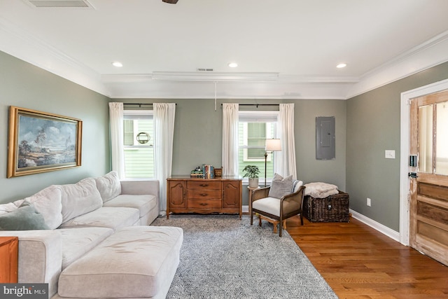 living room featuring recessed lighting, baseboards, ornamental molding, electric panel, and wood finished floors