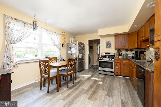 kitchen with appliances with stainless steel finishes, washer / clothes dryer, light wood-style floors, and brown cabinetry