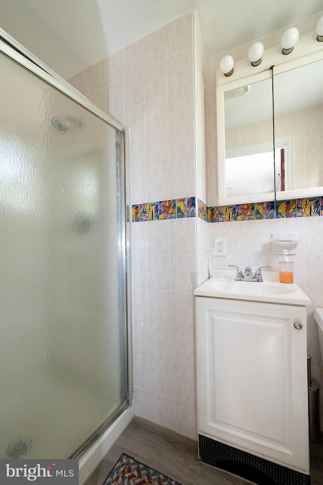 bathroom featuring tile walls, a stall shower, vanity, and wood finished floors