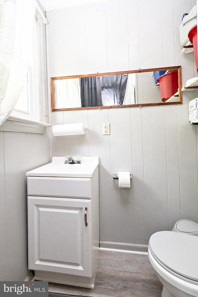half bath with wood finished floors, toilet, vanity, and baseboards