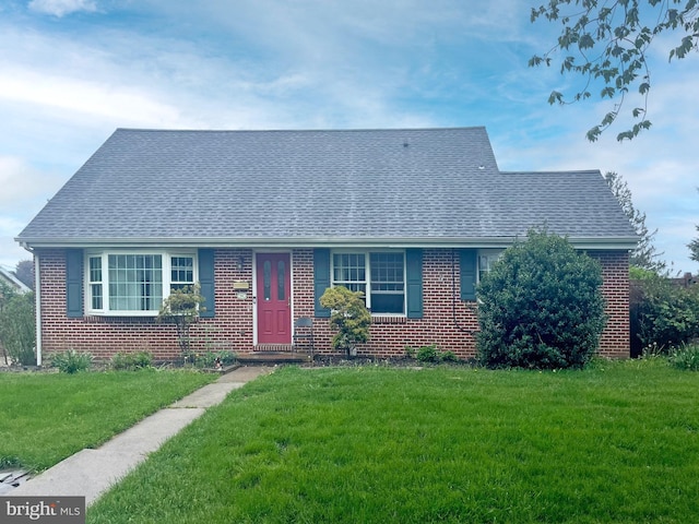 view of front of home with a shingled roof, brick siding, and a front lawn