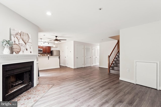 unfurnished living room with baseboards, stairway, ceiling fan, and light wood-style floors