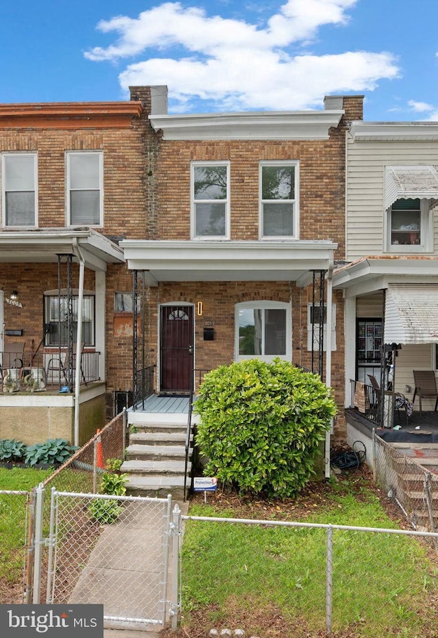 townhome / multi-family property featuring a gate, brick siding, covered porch, and a fenced front yard