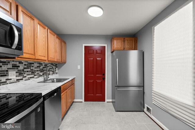 kitchen with stainless steel appliances, a sink, decorative backsplash, baseboards, and brown cabinetry
