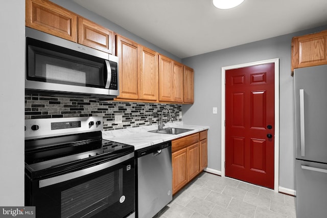 kitchen with appliances with stainless steel finishes, a sink, light countertops, decorative backsplash, and baseboards