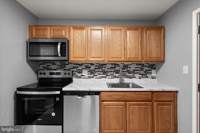kitchen featuring stainless steel appliances, a sink, tasteful backsplash, and light stone countertops