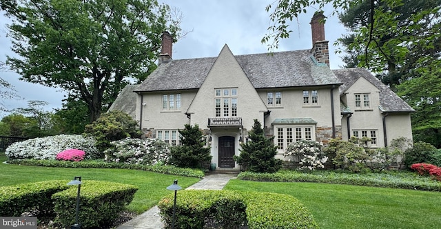 english style home with a front lawn, stucco siding, a chimney, and stone siding