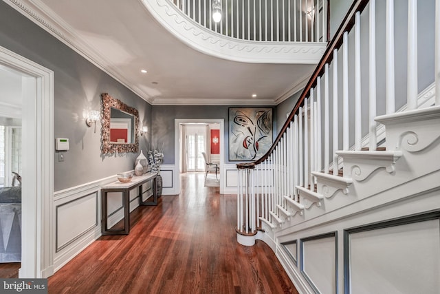 foyer entrance with a decorative wall, wood finished floors, ornamental molding, stairway, and wainscoting