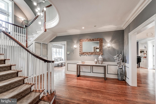 entrance foyer with crown molding, stairway, wood finished floors, and a wainscoted wall