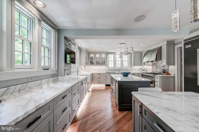 kitchen with high end appliances, wall chimney exhaust hood, light wood-style floors, a kitchen island, and tasteful backsplash
