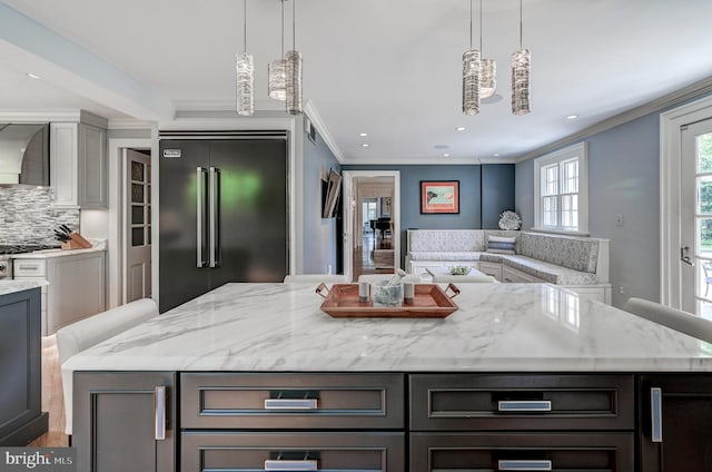 kitchen featuring light stone counters, crown molding, wall chimney range hood, tasteful backsplash, and high end refrigerator