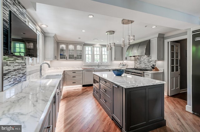 kitchen featuring light stone countertops, glass insert cabinets, a sink, backsplash, and wall chimney range hood