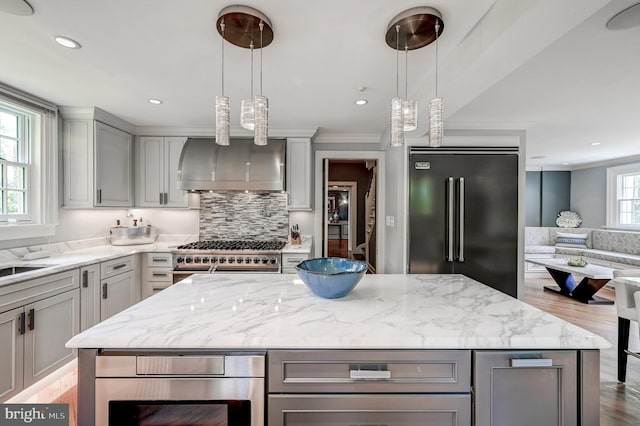 kitchen with wood finished floors, wall chimney exhaust hood, premium appliances, light stone countertops, and gray cabinetry