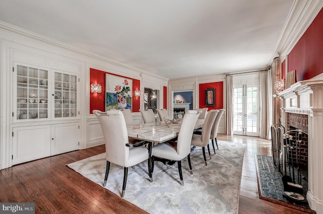 dining area with a decorative wall, french doors, wood finished floors, a fireplace, and crown molding