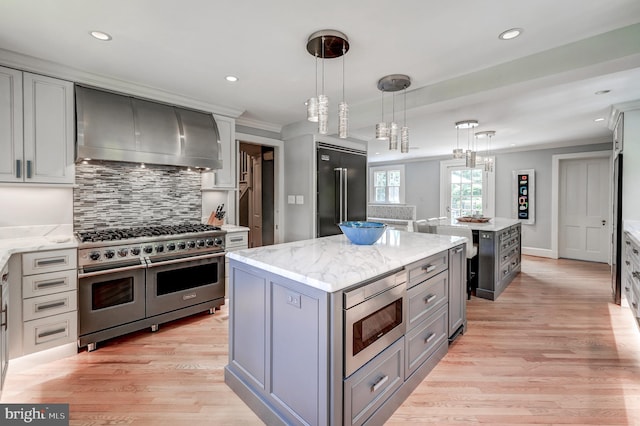 kitchen featuring a center island, ornamental molding, high end appliances, wall chimney range hood, and gray cabinets