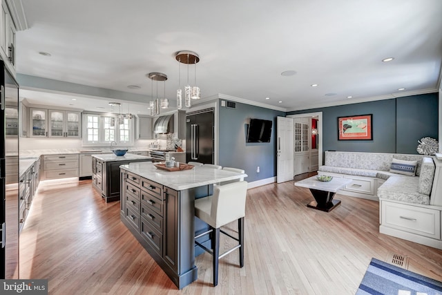 kitchen with decorative light fixtures, crown molding, light wood-style flooring, a center island, and high end appliances