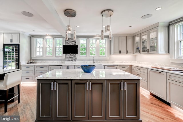 kitchen featuring light wood-style flooring, a center island, beverage cooler, glass insert cabinets, and hanging light fixtures
