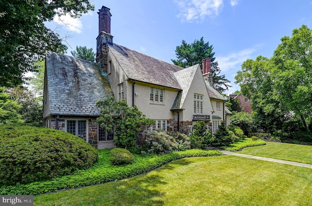 view of side of property featuring a high end roof, stone siding, a yard, stucco siding, and a chimney