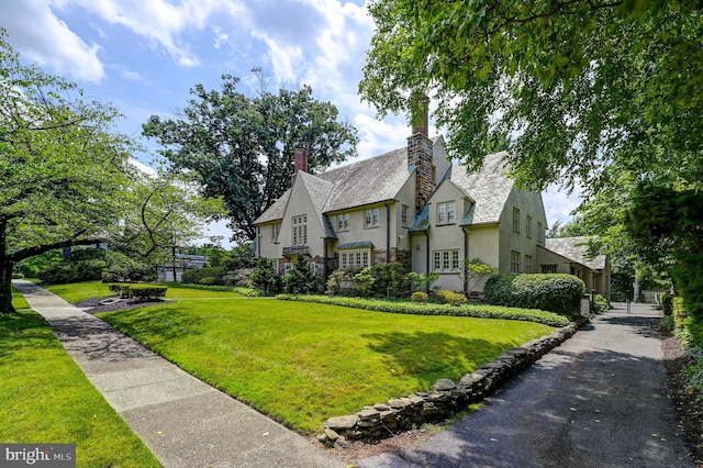 tudor home with a chimney, stucco siding, a front lawn, and stone siding