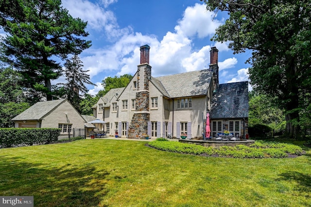 rear view of house featuring a lawn, a chimney, fence, a high end roof, and stone siding
