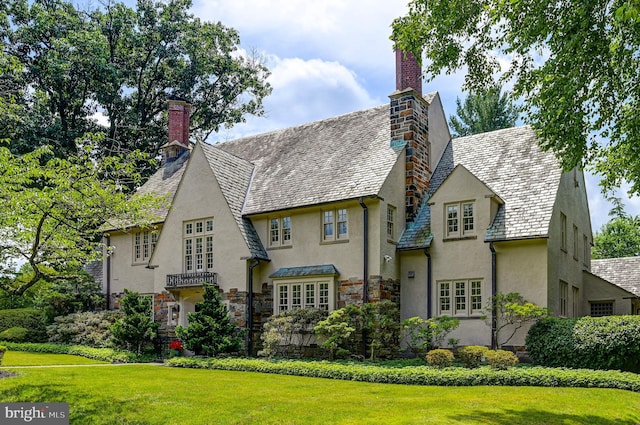 back of house with a high end roof, stone siding, a yard, stucco siding, and a chimney