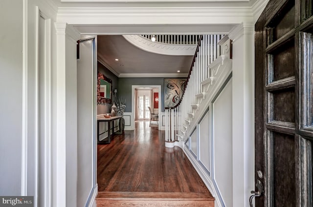 foyer with ornamental molding, wainscoting, stairs, a decorative wall, and wood finished floors