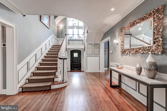 foyer entrance featuring stairway, ornamental molding, arched walkways, and wood finished floors
