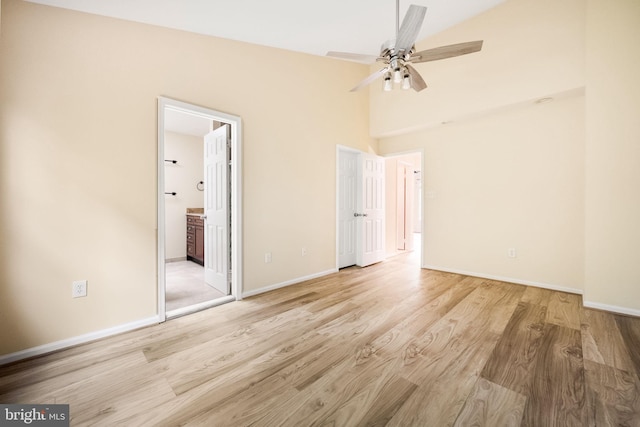 unfurnished bedroom with light wood-type flooring, a ceiling fan, connected bathroom, a high ceiling, and baseboards
