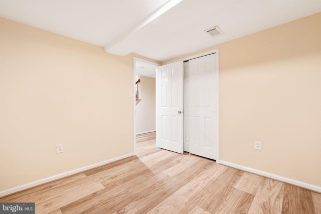 unfurnished bedroom featuring a closet, baseboards, visible vents, wood finished floors, and beamed ceiling