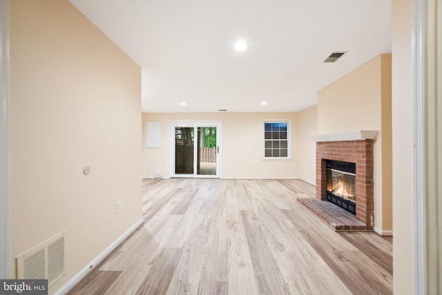 unfurnished living room featuring light wood-style floors, visible vents, baseboards, and a brick fireplace